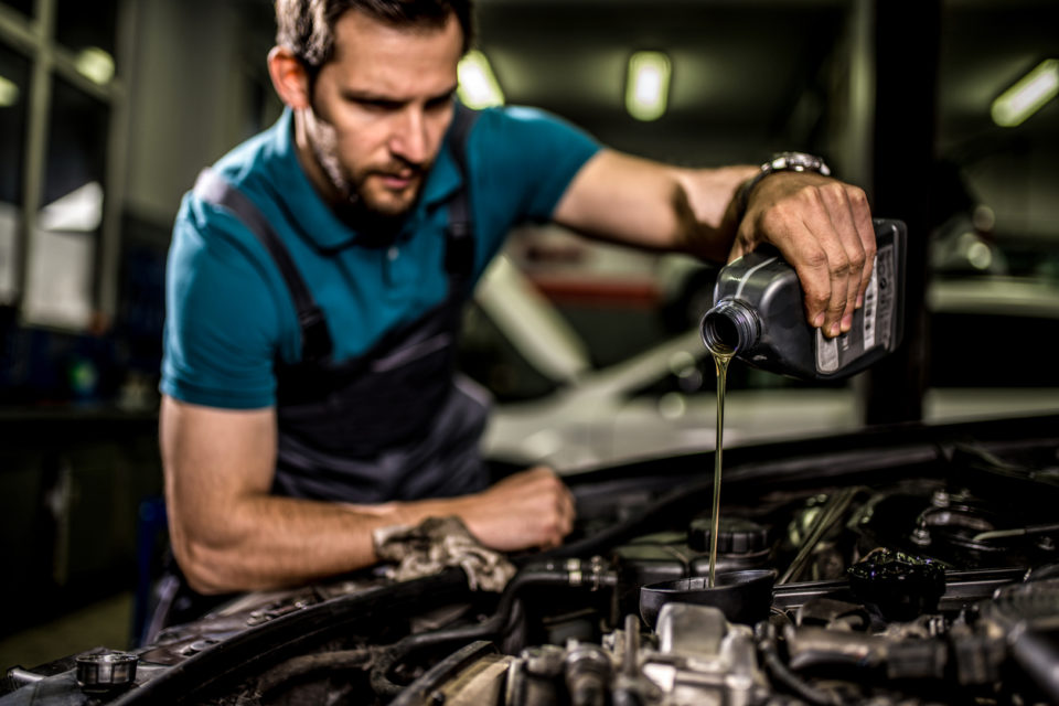 Mechanic changing oil on the vehicle at car workshop.